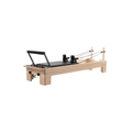 A Pilates reformer machine with a light natural wood frame, black padded carriage, black handlebar, and black resistance springs, shown on a plain white background.